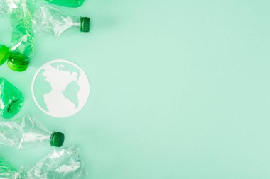 Yeşil arka planda buruşmuş plastik şişelerin yanındaki kağıt toprak tabelasının en üst görüntüsü, ekoloji kavramı