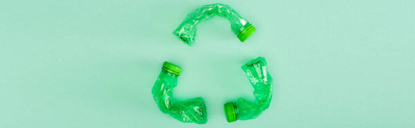 Panoramic shot of recycle sign from crumpled plastic bottles on green background, ecology concept
