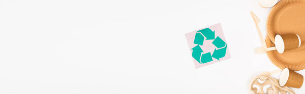 Horizontal image of disposable tableware near card with recycle sing on white background, ecology concept