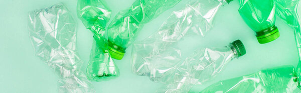 Горизонтальный урожай смятых пластиковых бутылок на зеленой поверхности, концепция экологии