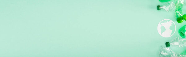 Horizontal crop of paper earth symbol and crumpled plastic bottles on green background with copy space, ecology concept