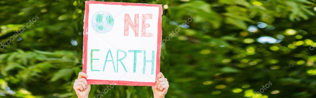 Horizontal concept of man holding placard with one earth lettering with trees at background, ecology concept