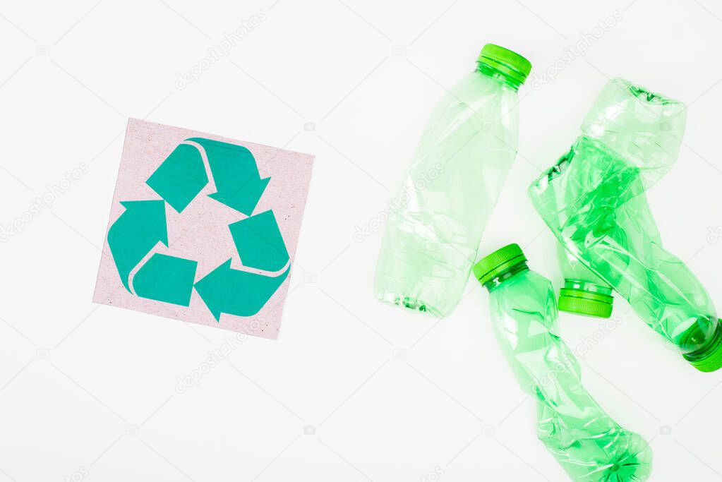 Top view of card with recycle sign near crumpled plastic bottles on white background, ecology concept