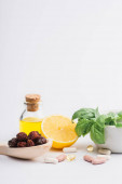 green leaves in mortar, berries and lemon near pills on white background, naturopathy concept
