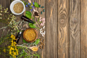 top view of pills in spoons, green herbs and wildflowers on wooden surface, naturopathy concept