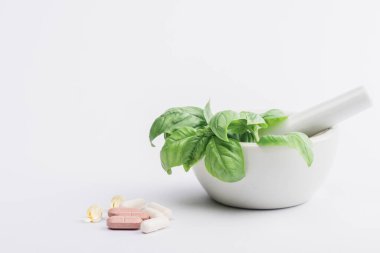 Beyaz arkaplandaki hapların yanında yeşil havan yaprakları, naturopati kavramı