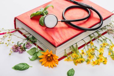 herbs in book with stethoscope on white background, naturopathy concept clipart