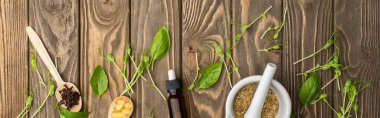 Kaşıklar, havan topları, yeşil otlar ve tahta yüzeyde şişe, naturopati konsepti.