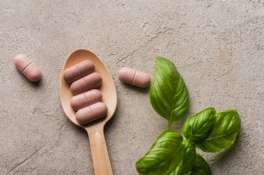 Yeşil yaprakların üst görüntüsü ve tahta kaşıkta haplar beton arka planda, naturopati konsepti