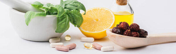 green leaves in mortar, berries and lemon near pills on white background, naturopathy concept