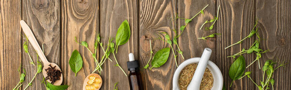 top view of pills in spoons, mortar, green herbs and bottle on wooden surface, naturopathy concept