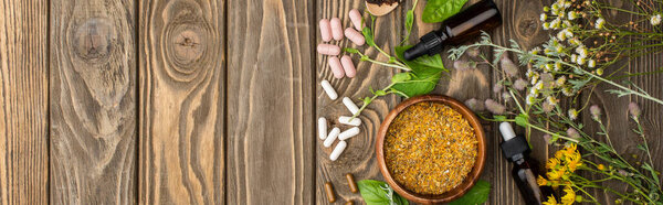 top view of pills, green herbs and wildflowers on wooden surface, naturopathy concept