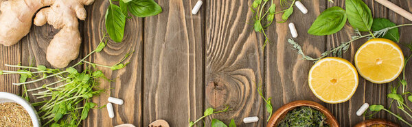 panoramic shot of pills and green herbs on wooden surface, naturopathy concept