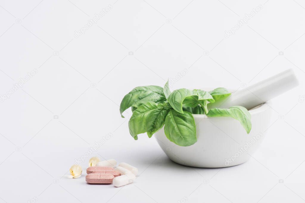 green leaves in mortar near pills on white background, naturopathy concept