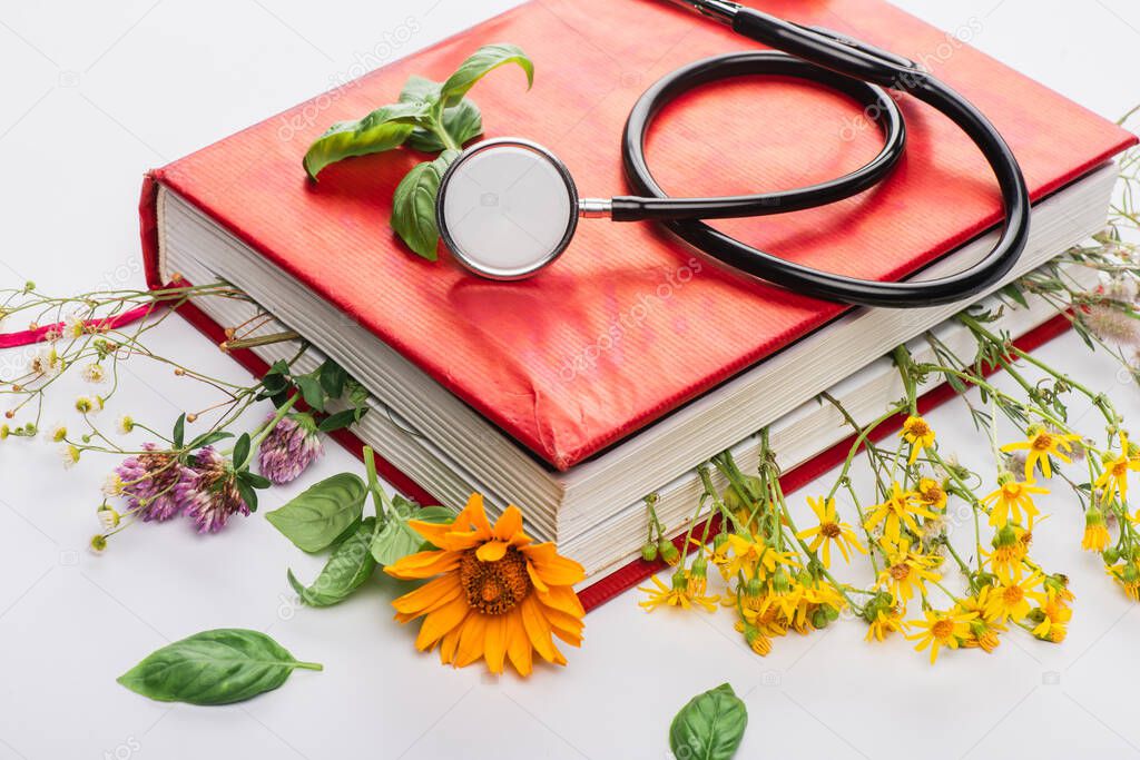 herbs in book with stethoscope on white background, naturopathy concept