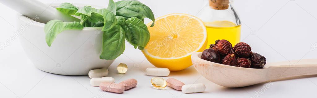 green leaves in mortar, berries and lemon near pills on white background, naturopathy concept