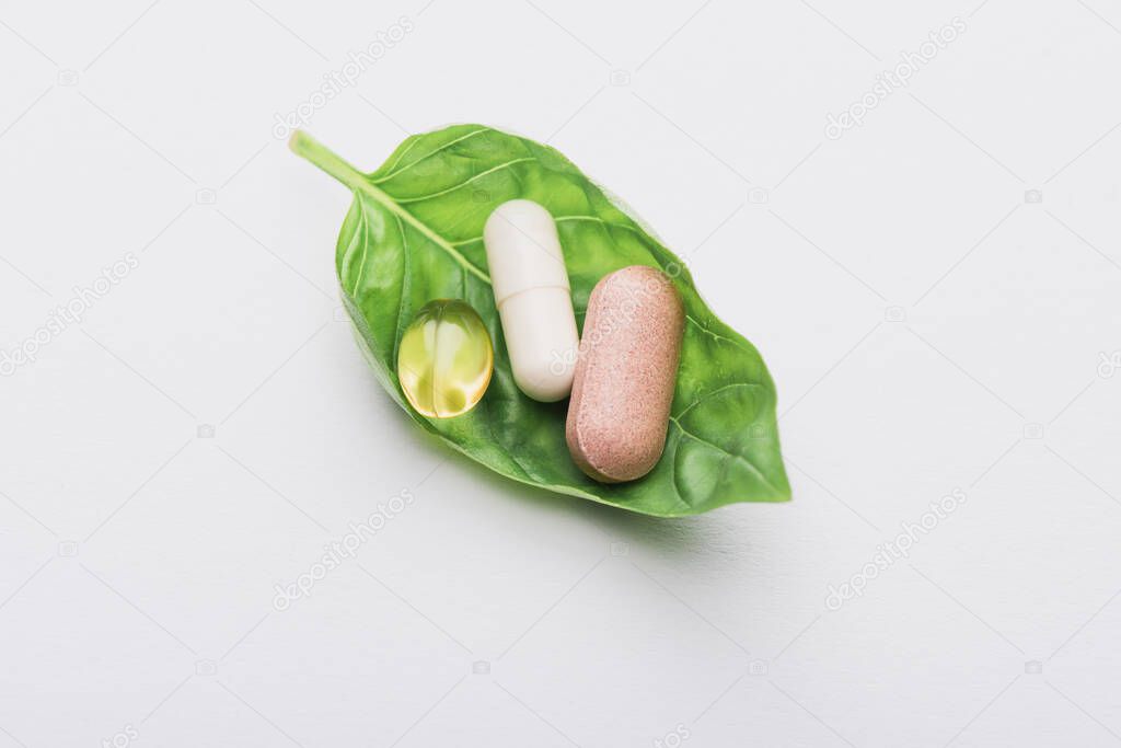 pills on green leaf on white background, naturopathy concept