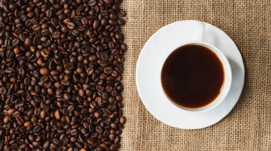top view of cup of coffee on saucer with coffee beans and sackcloth on background clipart