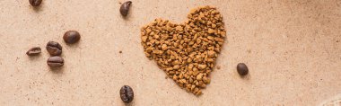 top view of heart made of instant coffee near coffee beans on beige surface, panoramic shot clipart