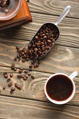 top view of vintage coffee grinder, metal scoop with coffee beans and cup on wooden surface clipart