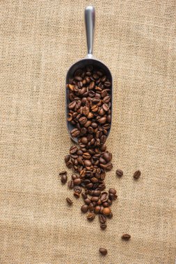 top view of metal scoop with coffee beans on sackcloth clipart