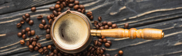 top view of cezve with coffee on coffee beans on wooden surface, panoramic shot