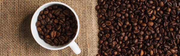 top view of cup with coffee beans and sackcloth on background, panoramic shot