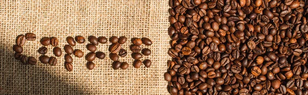 top view of coffee lettering made of beans in sunlight on sackcloth, panoramic shot