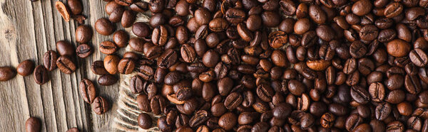 top view of coffee beans scattered on burlap on wooden surface, panoramic shot