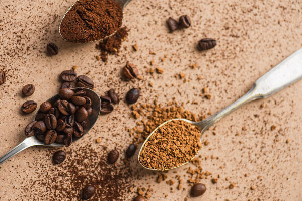 top view of ground, instant coffee and beans in spoons on beige surface