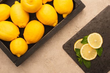 Kutuda sarı limonların üst görüntüsü ve bej beton yüzeyde yeşil nane yaprakları ile dilimlenmiş.