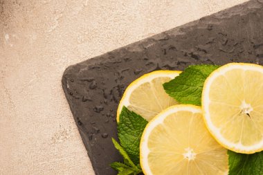 Nane yeşili yaprakların üst görüntüsü, bej beton yüzeyde siyah tahtada limon dilimleri.