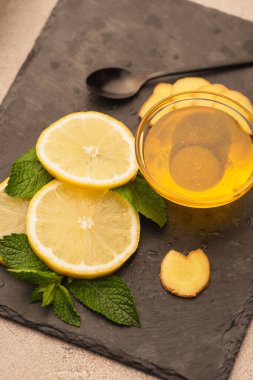 Nane yeşili yapraklar, zencefil kökü ve limon dilimleri ve siyah tahtada bal.