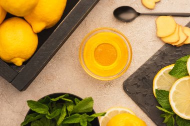 Sarı limon, nane yeşili yapraklar, zencefil kökü dilimleri ve bej beton yüzeyde bal.