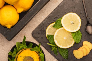 Sarı limonların üst görüntüsü, nane yeşili yapraklar ve bej beton yüzeyde bal