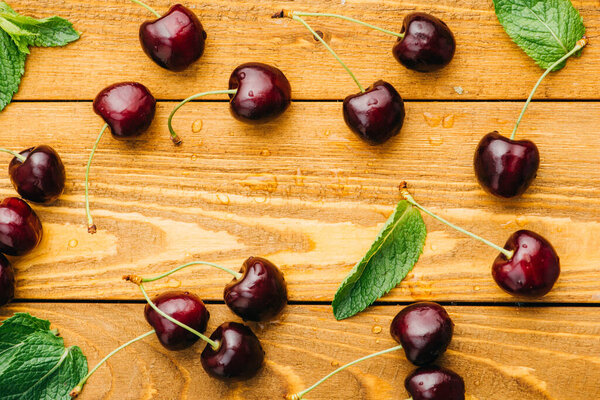 top view of wet ripe sweet cherries with green leaves on wooden surface