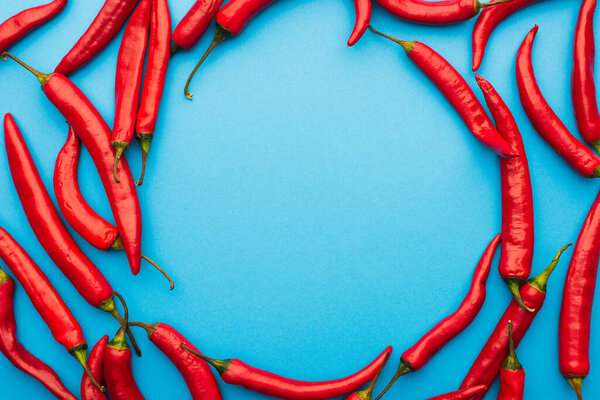 round frame made of spicy red chili peppers on blue background with copy space