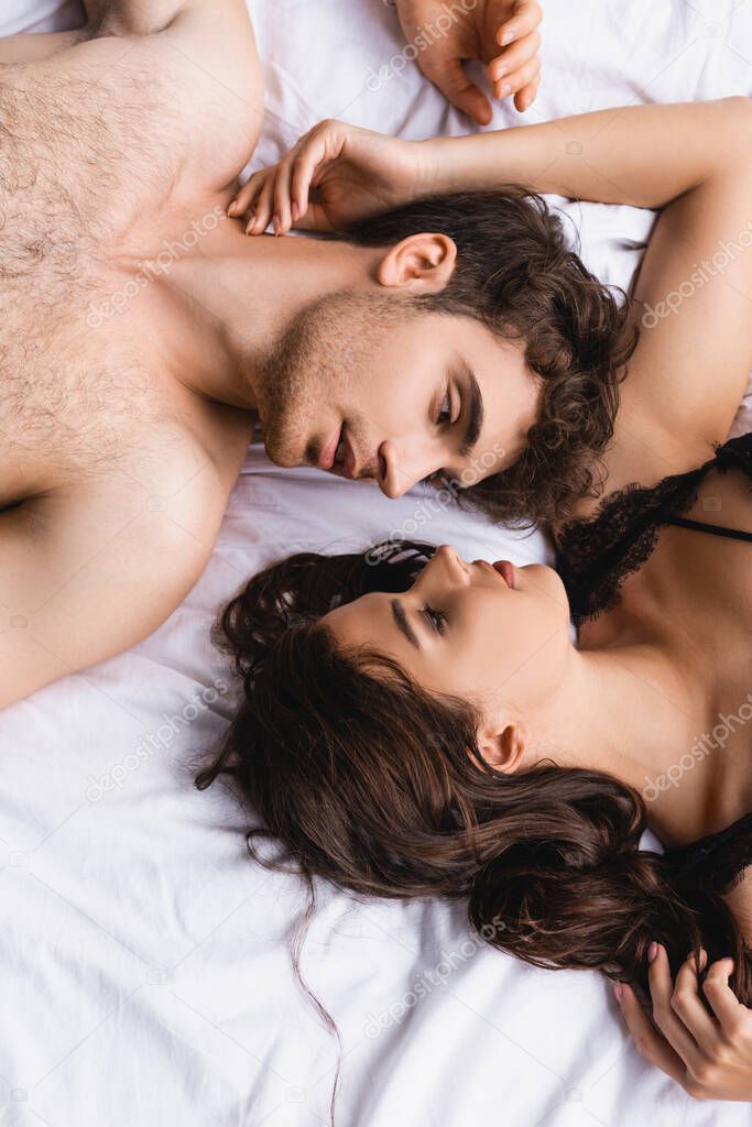 top view of shirtless man and woman in bra looking at each other on bed at home