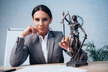 selective focus of lawyer in formal wear touching statuette of justice in office clipart