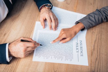 partial view of lawyer pointing with finger at insurance policy contract near businessman with pen clipart