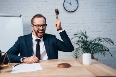 selective focus of excited judge in glasses and suit holding gavel  clipart