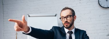 Gözlüklü ve takım elbiseli sakallı iş adamının ofiste parmağı olan panoramik ürünleri.