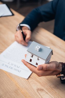 cropped view of lawyer holding house model near documents with insurance policy lettering on table  clipart