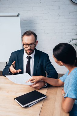 Gözlüklü, sakallı bir avukatın yakınındaki belgeye parmakla işaret eden müşterinin seçici odağı 