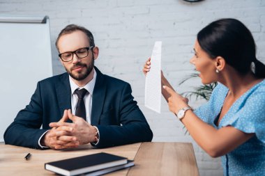 Gözlüklü, sakallı bir avukatın seçici odak noktası. Elleri sımsıkı oturup müvekkilinin yanında oturuyor. Ofisteki sözleşmeyi işaret ediyor. 