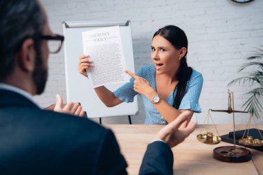 Hoşnutsuz ve esmer müşterinin seçici odağı gözlüklü avukatın yanındaki sigorta poliçesini işaret ediyor.