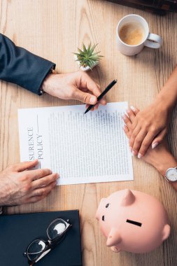 top view of lawyer holding pen near insurance policy agreement, piggy bank, plant and client  clipart