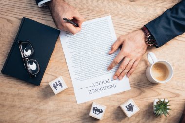 top view of lawyer signing insurance policy agreement near plant, glasses, notebook and wooden cubes with family, car and house clipart