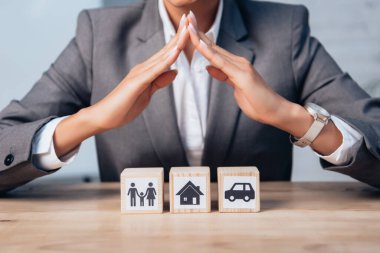 cropped view of lawyer holding hands above wooden cubes with family, car and house  clipart