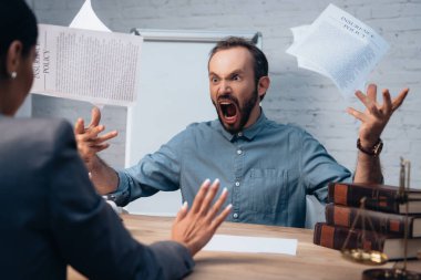 selective focus of angry and bearded man screaming while throwing in air documents near lawyer  clipart